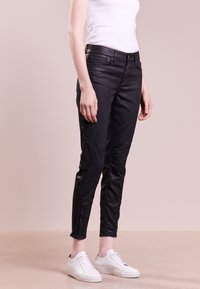 Svarta tajta jeans med en slät yta och dragkedjedetaljer vid fållen, med sidopaneler och en klassisk fem-fickorsdesign, i kombination med vita sneakers.