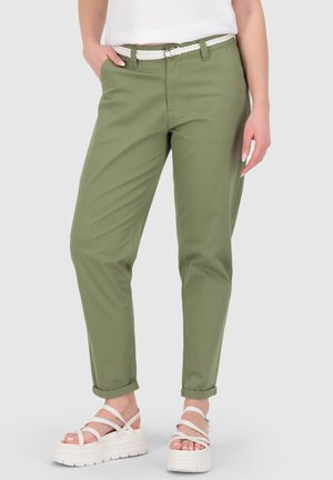 Person wearing olive green cuffed pants with white braided belt and white platform sandals, standing with one hand in pocket.