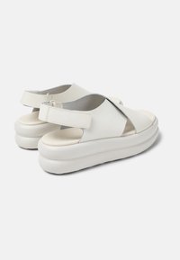 I sandali bianchi in pelle presentano un design aperto con una larga fascia sul piede, una fascia posteriore e una spessa suola piattaforma bianca.