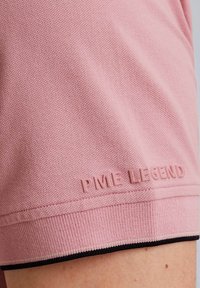 Chemise polo rose en tissu texturé, dotée d'un logo "PME LEGEND" en caoutchouc et d'une bordure contrastante noire et blanche à l'ourlet.