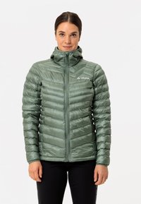 Groene synthetische pufferjack met verticale stiksels, hoge kraag, ritssluiting aan de voorkant en logodetail op de linkerkant van de borst. Glad, glanzend textuur.