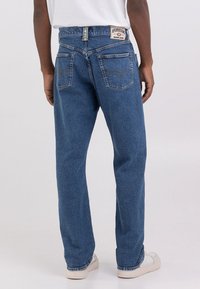 Jeans de mezclilla azul claro con corte recto, que cuentan con dobles bolsillos traseros y una etiqueta en la cinturilla. Tela texturizada y detalles de costura sutiles.