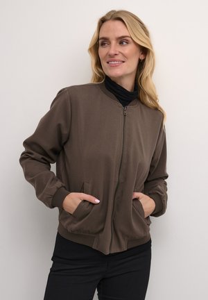Brown bomber jacket with a zip front, ribbed cuffs, and side pockets, made from smooth fabric, paired with a black turtleneck.