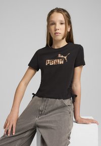 Camiseta negra de manga corta con un gráfico beige y marrón del logo "PUMA" y un diseño de gato. Presenta lazos en los laterales para un ajuste ajustable.