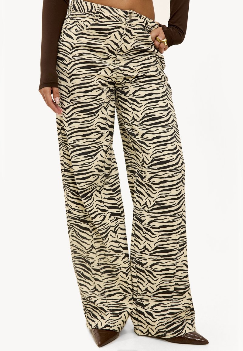Pantalons larges en tissu beige arborant un audacieux motif rayé noir de tigre. Fini avec une taille haute et des détails de couture subtils.
