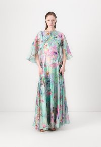 Langes, fließendes Kleid aus transparenter Stoff in Grüntönen, mit floralen Mustern in Rosa und Lila, und weiten, capeähnlichen Ärmeln.