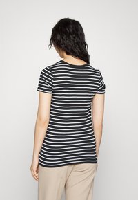 Camiseta de manga corta a rayas blancas y negras con cuello redondo, hecha de una tela suave, con un diseño ajustado y un dobladillo recto.