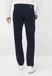 Marineblauwe denim jeans met een rechte snit, voorzien van een achterbandpatch, twee achterzakken en een nette afwerking. G gedragen met witte schoenen.