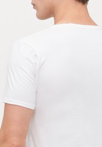 T-shirt en coton blanc à manches courtes, avec un col rond et une texture lisse, présenté de dos avec une légère vue d'épaule.
