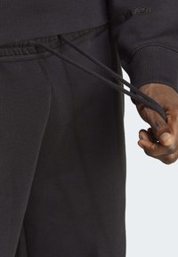 Felpa nera con cappuccio, maniche a costine, cordini e tasca visibile. Il tessuto è morbido e ha una texture liscia con un branding sottile.