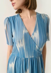 Vestido azul y blanco con un estampado, mangas cortas abullonadas, escote en V profundo y falda con pliegues. La tela parece suave con rayas verticales.
