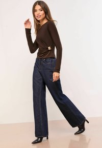 Pruun pika varrukaga pluus külgse kortsutatud detaili ja kuldse riistvaraga, kombineeritud kõrge vöökohaga tumesiniste laiade säärega teksadega ning mustade teravate kontsadega.