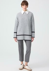 Grijze geribbelde trui met een witte kraag, gecombineerd met slanke grijze broek en beige sneakers. Bevat zwarte accenten aan de zoom en de manchetten.