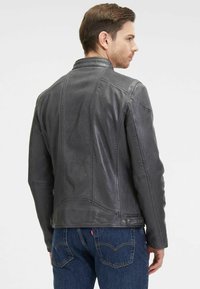 Giubbotto in pelle grigio con un design aderente, cuciture evidenziate e colletto strutturato, abbinato a jeans blu. Tessuto liscio e sottile lucentezza.