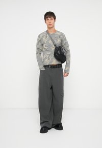 Cămașă gri cu camuflaj cu mânecă lungă, pantaloni lărguți gri cu dungi, brâu negru și geantă neagră de umăr cu design texturat. Încălțăminte neagră masivă.