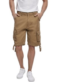 Shorts cargo beiges, fabriqués en tissu durable avec plusieurs poches, ourlets noués et coupe décontractée. Associés à des baskets blanches.