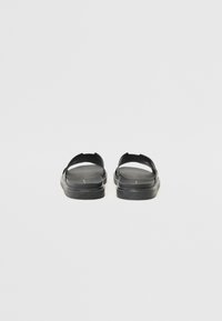 Sorte sandaler med flate såler, åpen tå og åpninger på siden. Laget av glatt materiale med minimalistisk design og uten synlige dekorasjoner.