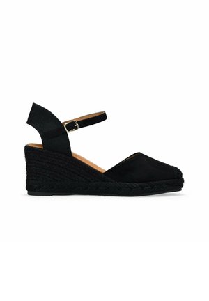 Espadrille negra de cuña con parte superior de tela, una correa en el tobillo con un hebilla de metal y una suela envuelta en yute texturizado.