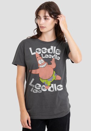 Young woman touching her hair wearing a dark gray T-shirt with a smiling cartoon starfish and the words "Leedle Leedle Leedle lee".