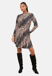 Šaty s kvetinovým vzorom, dlhé rukávy, čierny základ, ružové a žlté kvety, priliehavý pás, splývavá sukňa, doplnené čiernymi čižmami po kolená.