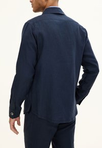 Navy blue linen shirt with a collar, long sleeves, and buttoned cuffs. Features a straight cut and side slits for ease of movement.