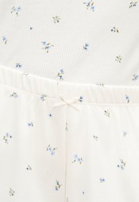 Κρεμ υφασμάτινο με ρίγες, λεπτά μπλε λουλουδάτα σχέδια και ελαστική μέση με μικρό δεμένο φιόγκο στο κέντρο μπροστά.