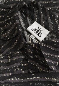 Fekete és szürke absztrakt csíkozott galléros ing, mérettel ellátott címkével: EU 38, US 8, valamint a márka logójával.