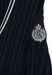 Navy blue cable-knit fabric with white double stripe detail and embroidered Polo Club crest patch featuring crown and laurel wreath.