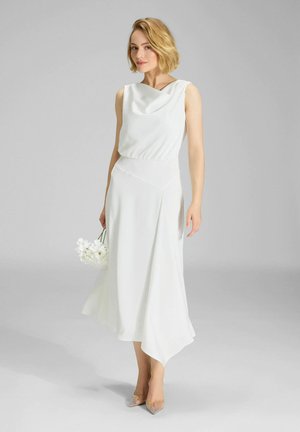 Robe blanche avec un col bénitier, un corsage ajusté et un ourlet asymétrique. Tissu léger et drapé subtil. Accentuée par des talons transparents.