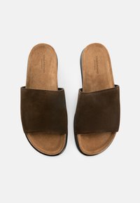 Καφέ σανδάλια slide από σουέντ με φαρδιά λωρίδα πάνω από το πόδι, μαλακή εσωτερική επένδυση και μαύρη ελαστική σόλα, με μινιμαλιστικό σχεδιασμό.