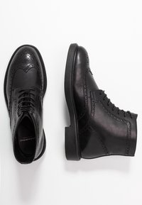 Černé kožené brogue boty s propracovaným perforovaným detailem, zaoblenou špičkou, plochou podrážkou a šněrováním. Hladká textura a klasický design.