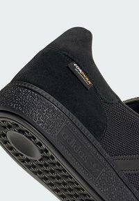 Czarny sneaker wykonany z siateczki i zamszu, z teksturowaną gumową podeszwą i etykietą Cordura po boku dla większej trwałości.