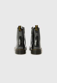 Botines de tobillo de purpurina negra con un acabado suave, que cuentan con cremalleras en la parte trasera, etiquetas de la marca amarillas y una suela robusta y texturizada.