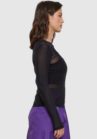 Schwarzes Langarmoberteil mit transparenten Einsätzen, gerundetem Ausschnitt, tailliertem Design und glatter Textur, kombiniert mit einem lila Rock.