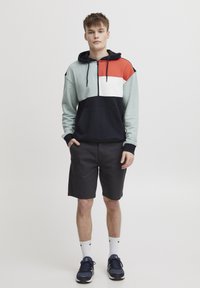 Hettegenser med fargeblokkdesign i grønn, rød og hvit, kombinert med sorte shorts. Inkluderer frontlomme og snor.