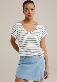 Randig V-ringad t-shirt i vitt och mörkgrönt, tillsammans med en ljusblå denimkjol med omslagsdesign och sidficka.