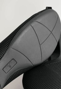 Schwarze Netzschuhe mit einer strukturierten Oberseite und einer Gummisohle mit gewölbtem Design und horizontalen Rillen für besseren Halt.