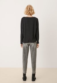 Svart långärmad topp med avslappnad passform, rundad halsringning och mjuk textur, kombinerad med ljusgrå raka jeans och svarta ankelstövlar.