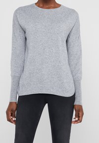 Pull tricot gris clair avec un col rond, des manches longues et des poignets côtelés. Texture douce et ourlet légèrement arrondi.