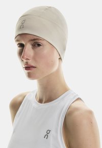 Casquette de performance beige clair avec un design sans couture. Fabriquée en tissu extensible, elle présente un petit logo sur le devant et une texture lisse.
