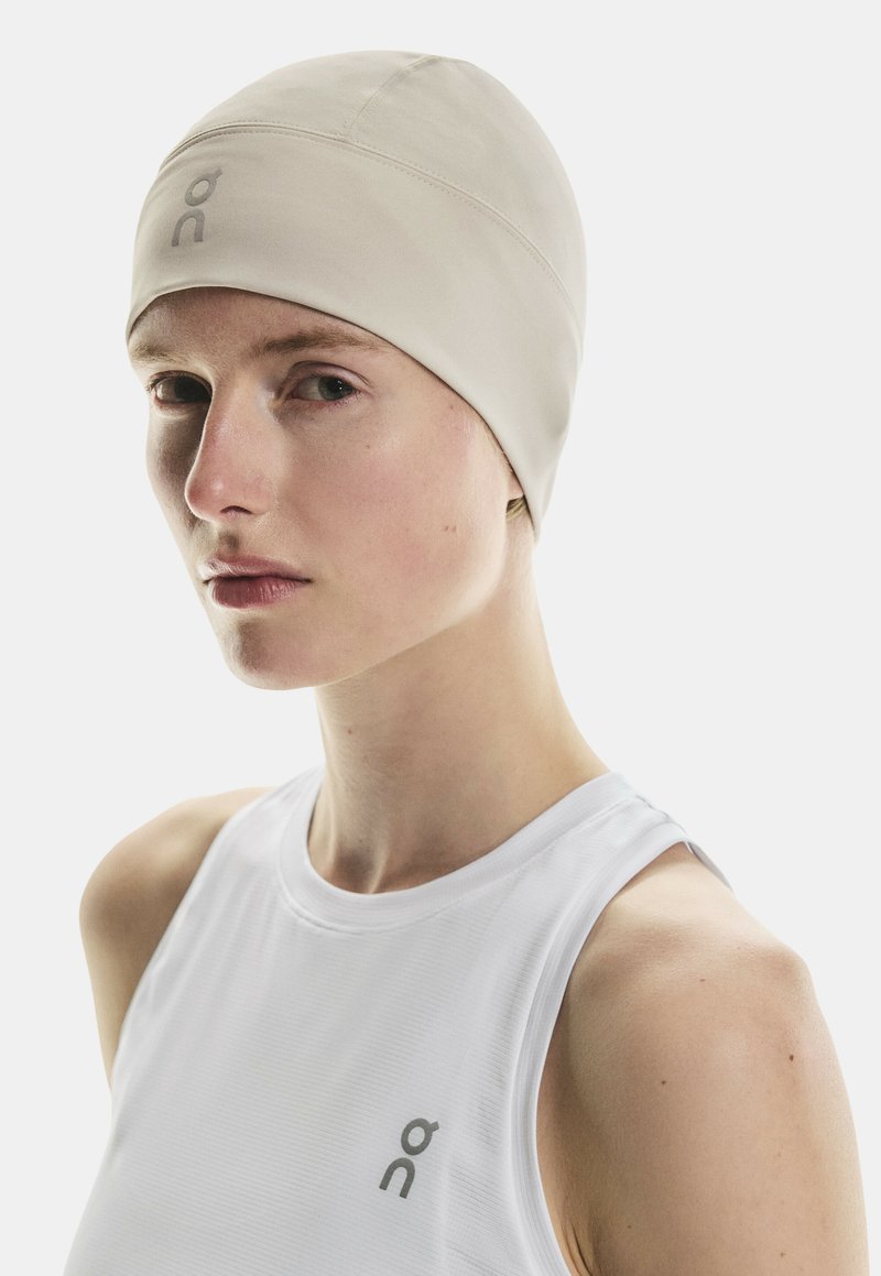 Casquette de performance beige clair avec un design sans couture. Fabriquée en tissu extensible, elle présente un petit logo sur le devant et une texture lisse.