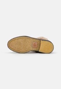 Bota de ante color marrón claro con suela de goma, que presenta un patrón texturizado y una etiqueta de cuero marrón en el talón. Diseño robusto y adaptable.
