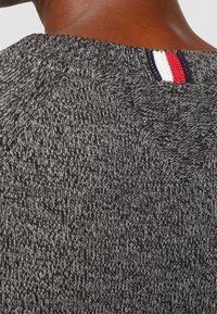 Dunkelgrauer gestrickter Pullover mit einem strukturierten Muster, das am hinteren Kragen eine kontrastierende rot-weiß-blaue Linie aufweist.