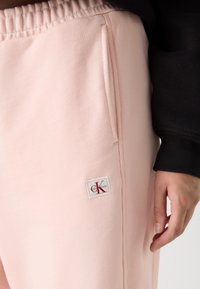 Jogging en coton rose avec une taille élastique, des poches latérales et un patch logo Calvin Klein rouge et blanc. Tissu texturé.