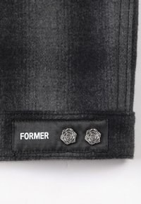 Tissu en feutre noir avec une texture lisse, comportant une étiquette portant la mention "ANCIEN" et deux accents métalliques en forme de rose.