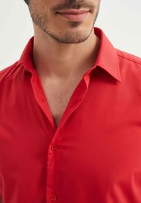 Chemise rouge à boutons avec une texture lisse, col classique, et trois boutons visibles. Le tissu semble léger, adapté aux temps chauds.