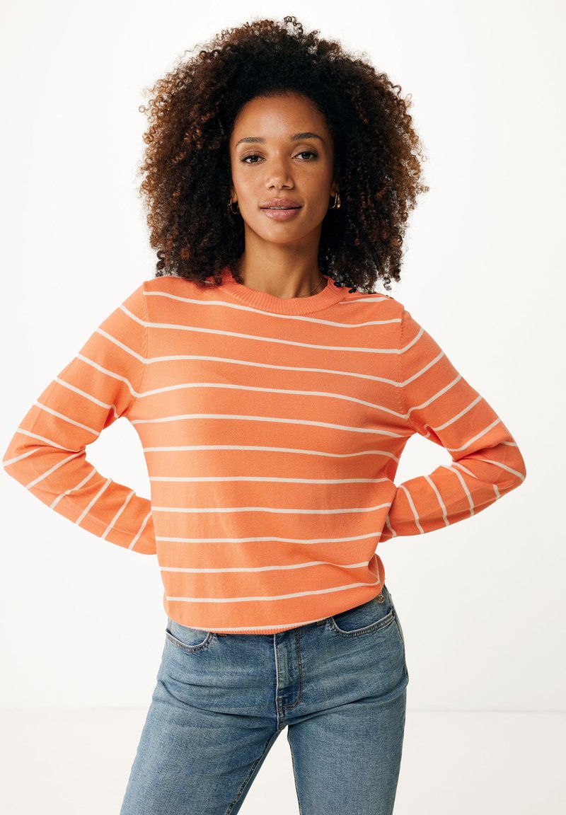 Pomarańczowy sweter w paski z długimi rękawami i okrągłym dekoltem, z białymi paskami i strukturalnym splotem. W połączeniu z niebieskimi dżinsami.