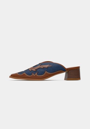 Denim slip-on mules with a pointed toe, brown leather accents, and detailed stitching in a wave pattern. Low, stacked wooden heel.