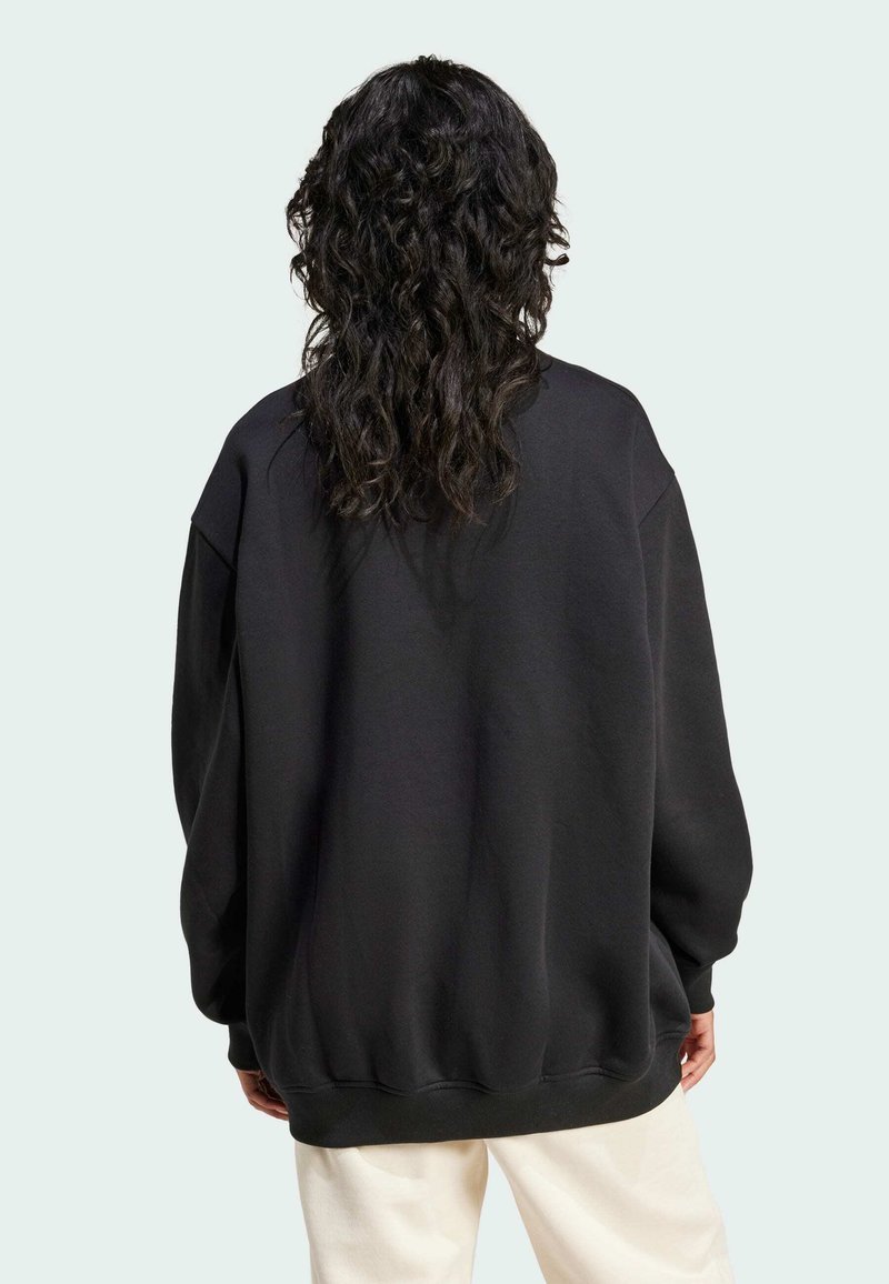 Sort oversized sweatshirt med rund halsudskæring, sænket skulder, og ribkanter, lavet af blødt stof med en glat struktur.
