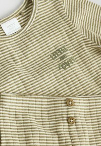 Gestreepte babyoutfit in beige en gebroken wit, met gebreide stof, ronde halslijn en twee bruine knopen met het "NEXT" merk.